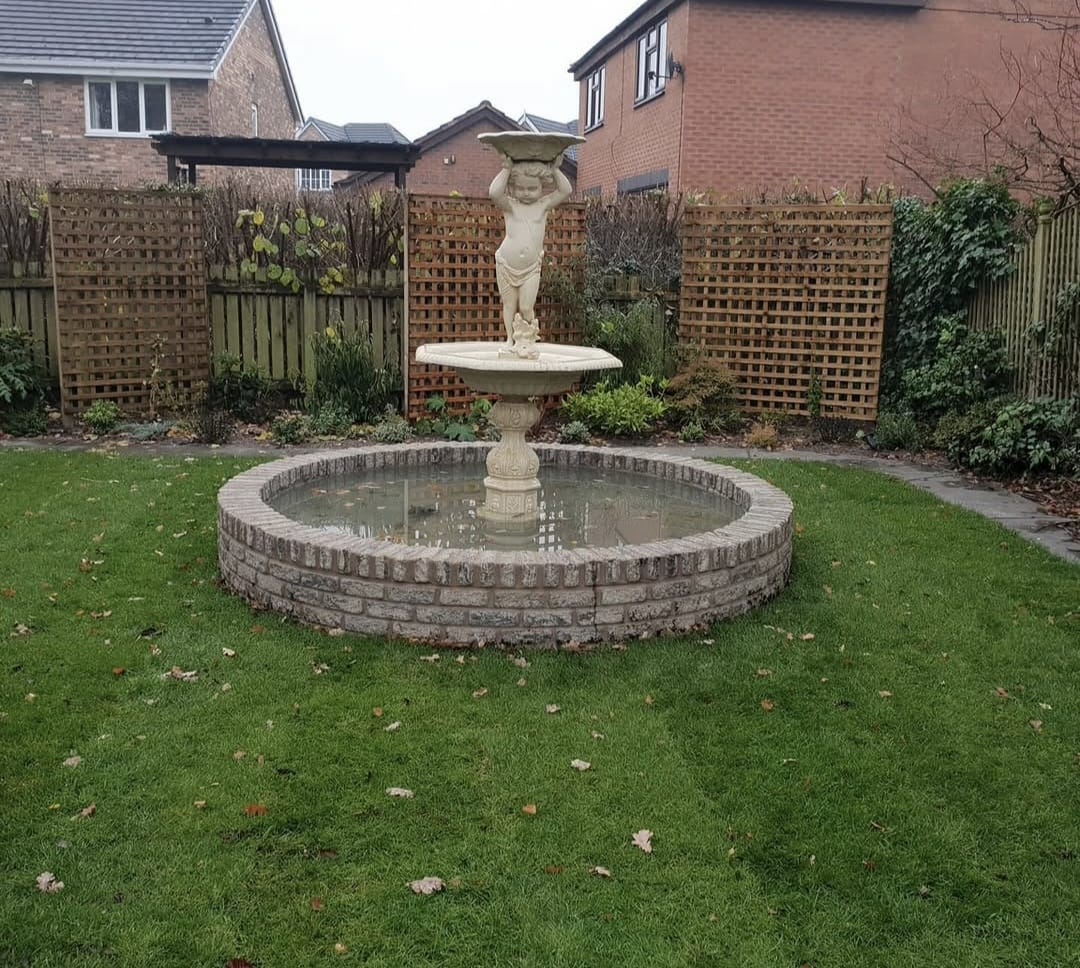 Classical fountain set within a circular brick-edged pond and lawn by Rose Gardens